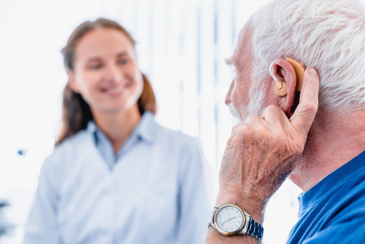 Man with hearing aid receiving care from audiologist.