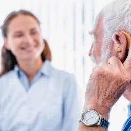 Man with hearing aid receiving care from audiologist.
