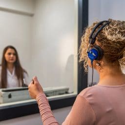 A woman gets an audiology test inside a sound booth.