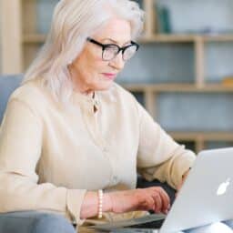 Older woman in glasses working on her laptop.